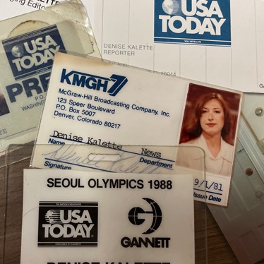 An assortment of media credentials and memorabilia including a USA Today newspaper header, a business card from KMGH-TV, and a press pass for the Seoul Olympics 1988, all belonging to Denise Kalette.